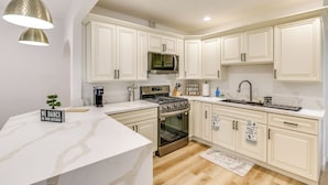 A modern kitchen with white cabinetry, stainless steel appliances, and a marble countertop.