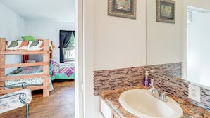 A bedroom with a wooden bed, a window with curtains, and a bathroom with a sink and tiled backsplash. - Arkansas Cabin w/ Deck < 1 Mi to Norfork Lake (Henderson)