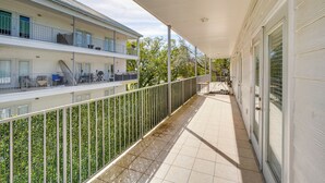 A covered balcony with a metal railing, a tiled floor, and a building with multiple windows and balconies.