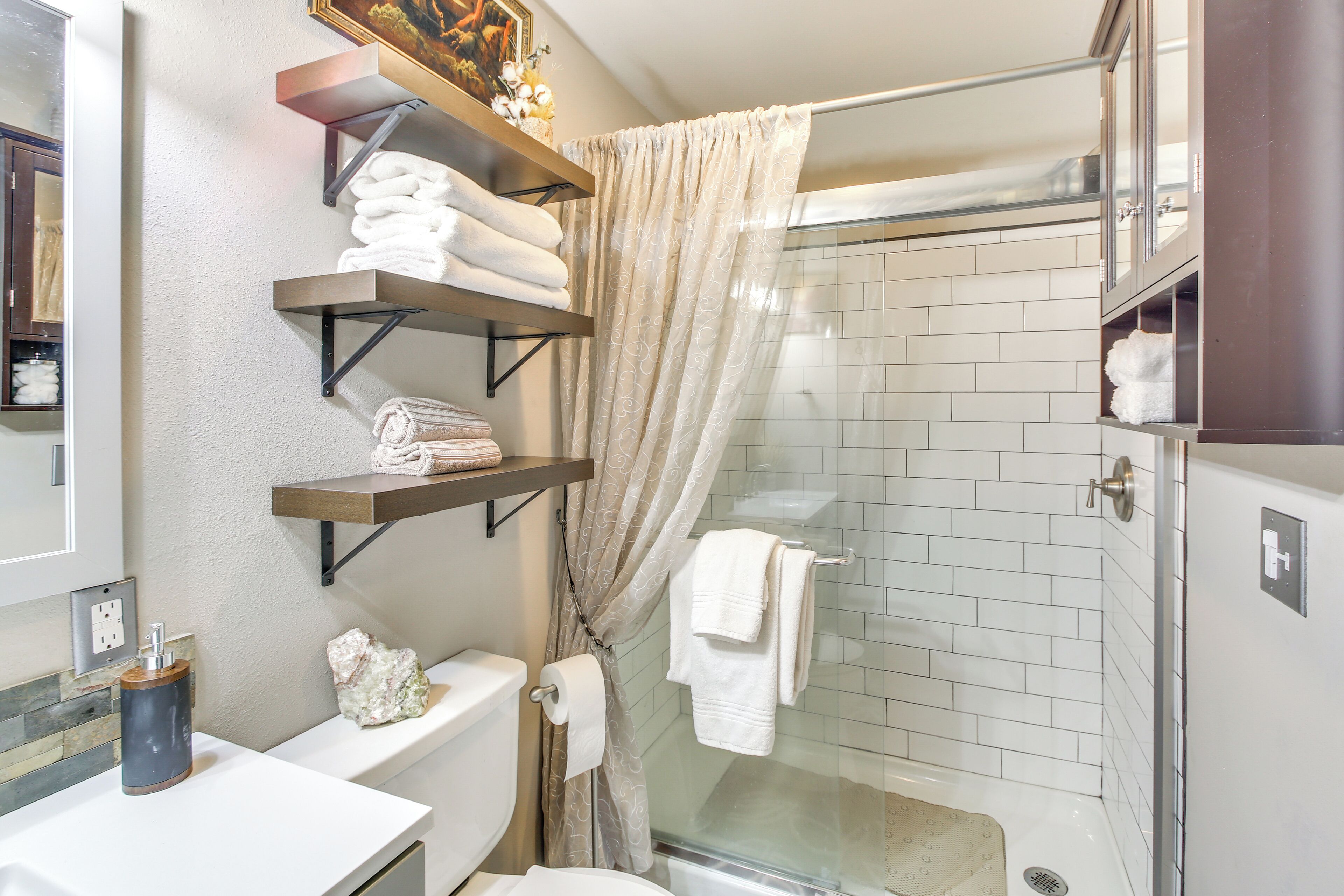 Ein modernes Badezimmer mit einer Duschkabine aus Glas, weißen Fliesen und Regalen für Handtücher.