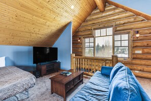A log cabin interior with a wooden ceiling, a large window, a television, a sofa, and a coffee table.