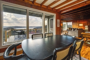 Un vaste espace dédié à la salle à manger, avec une grande table et des chaises, de grandes fenêtres offrant une vue sur l’extérieur, et un coin salon confortable avec un canapé et une table.