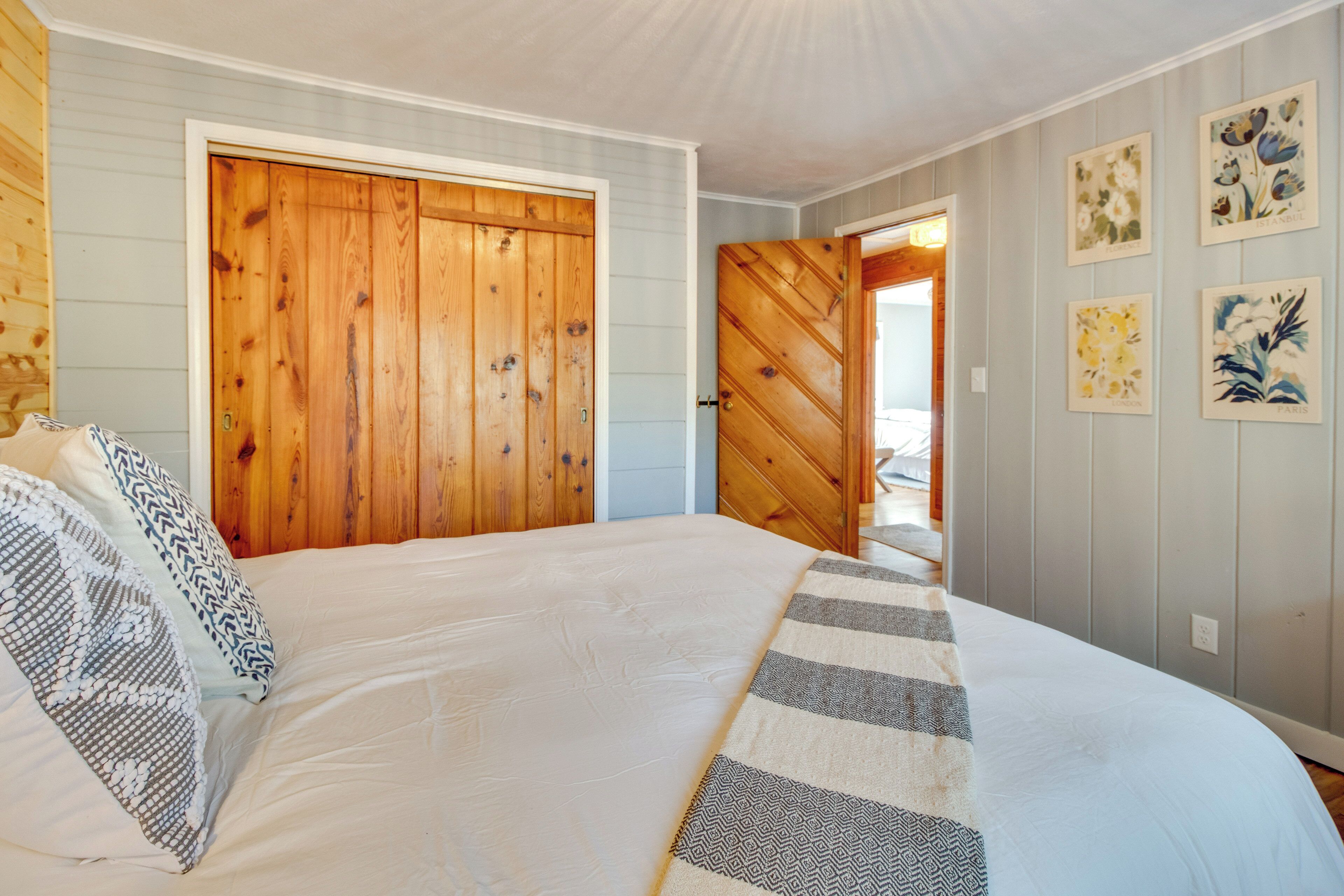 A bedroom with a large bed, wooden doors, and a hallway with framed pictures.