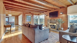 Un salon spacieux doté d’une cheminée, de parquets en bois et de grandes fenêtres.
