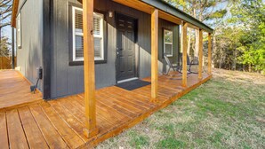 A wooden deck with a black door and windows, surrounded by a grassy area with trees. - Cozy Henderson Studio - 2 Mi to Norfork Lake! (Henderson)