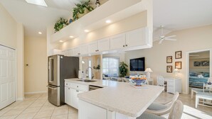 A modern kitchen with white cabinetry, a stainless steel refrigerator, and a central island with chairs.