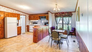 A kitchen with wooden cabinets, a refrigerator, a dining area with chairs, and a window with curtains. - 'valley View Lodge' Rural Home in Bridgeport! (Bridgeport)