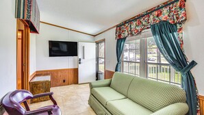 A living room with a green patterned sofa, a wooden chair, a flat-screen TV mounted on the wall, and a window with a floral curtain. - 'valley View Lodge' Rural Home in Bridgeport! (Bridgeport)