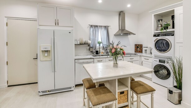 A modern kitchen with white cabinetry, a built-in washing machine, and a dining area with a table and benches.