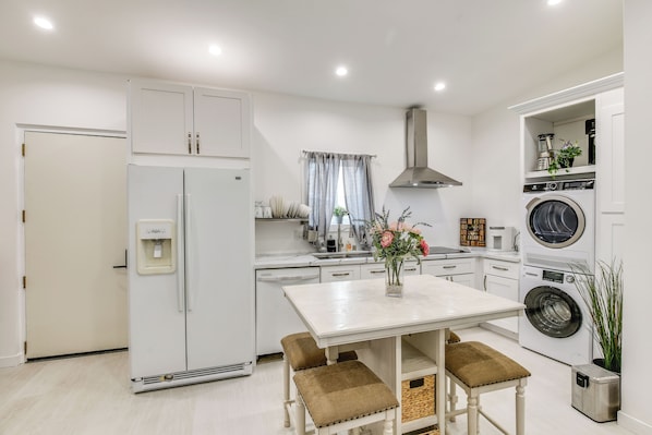 Uma cozinha moderna com armários brancos, máquina de lavar embutida e um espaço de refeições com mesa e bancos.