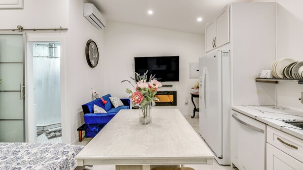 A modern kitchen with white cabinetry, a dining table with a vase of flowers, a blue sofa, and a flat-screen TV mounted on the wall.