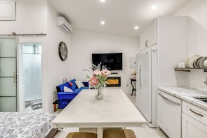 Uma cozinha moderna com armários brancos, uma mesa de jantar com um vaso de flores, um sofá azul e uma televisão de tela plana na parede.