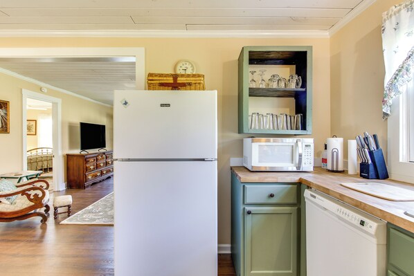 Una cocina equipada con refrigerador, microondas y lavavajillas. Hay una mesa de comedor de madera con sillas y un banco. Una cesta de mimbre está encima del refrigerador.