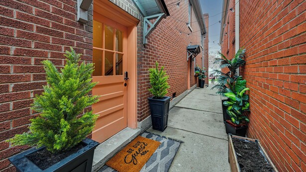 Une ruelle étroite aux murs de briques, avec une porte en bois et des plantes en pot.