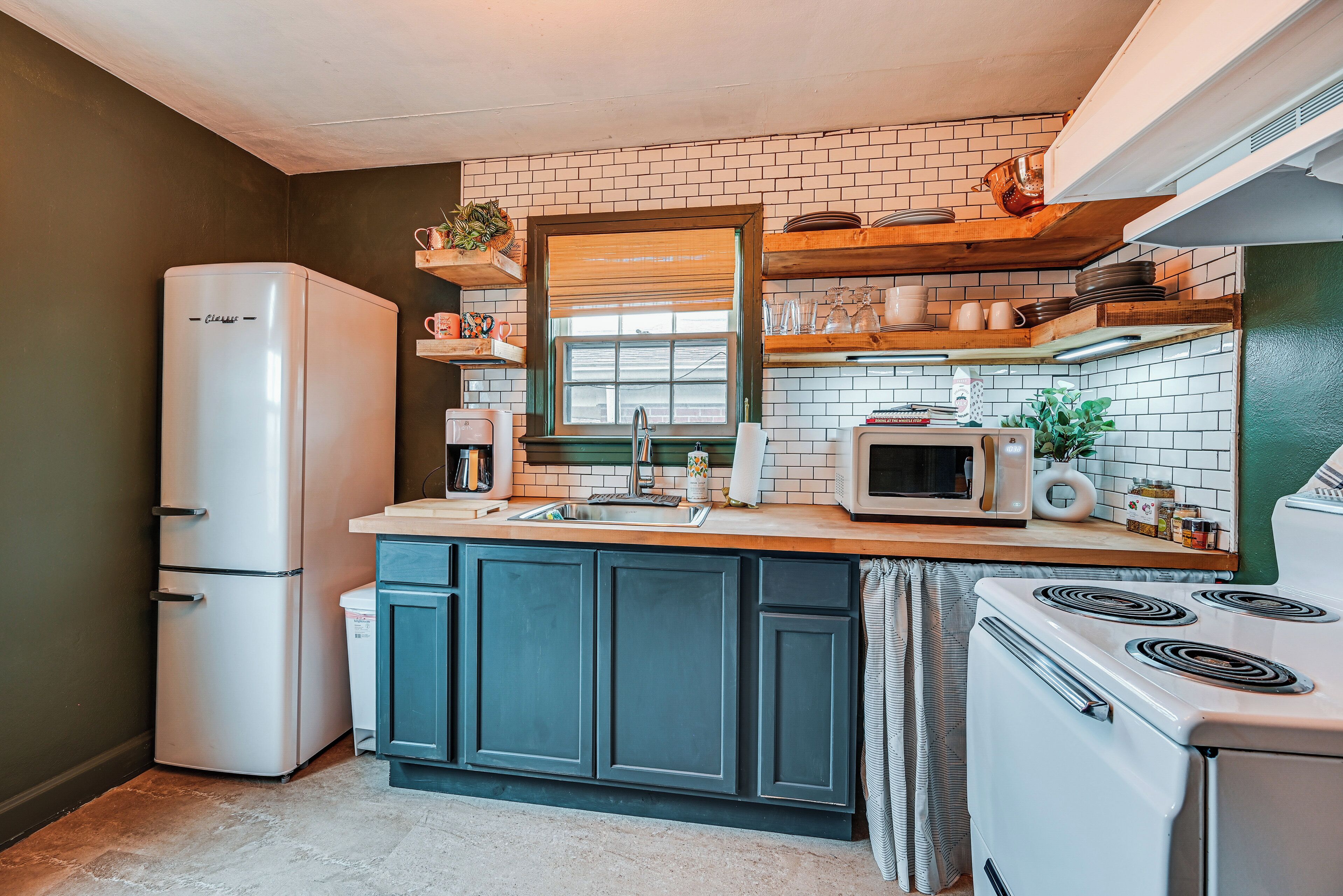 A compact kitchen with a refrigerator, stove, microwave, and a window with blinds.