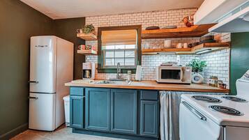 A compact kitchen with a refrigerator, stove, microwave, and a window with blinds.