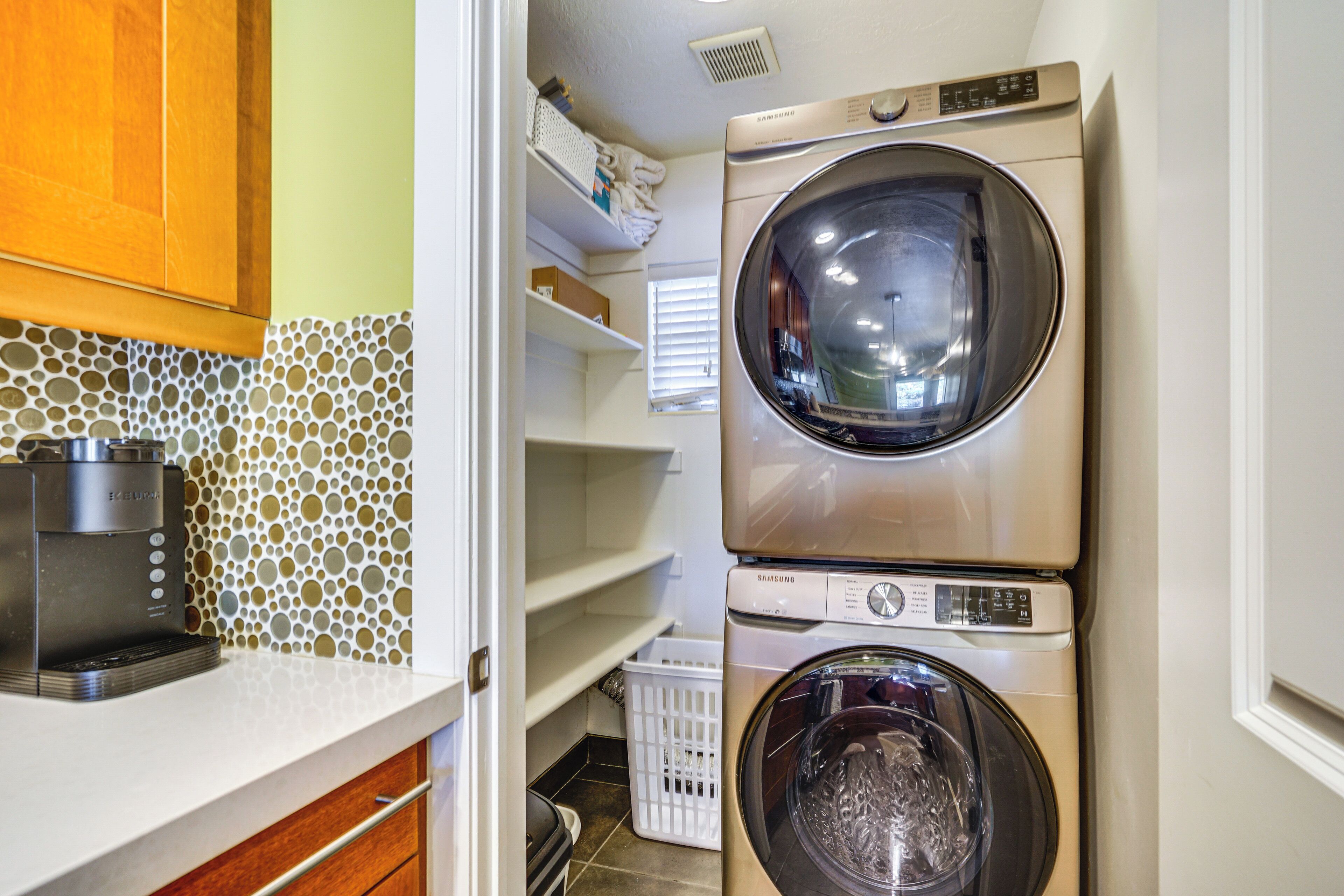 A laundry area with two stacked washers and dryers, a coffee maker, and a tiled backsplash.