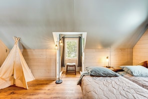 Um quarto de sótão acolhedor com piso de madeira, uma cama com travesseiros, um banquinho pequeno, um abajur e uma tenda indiana.