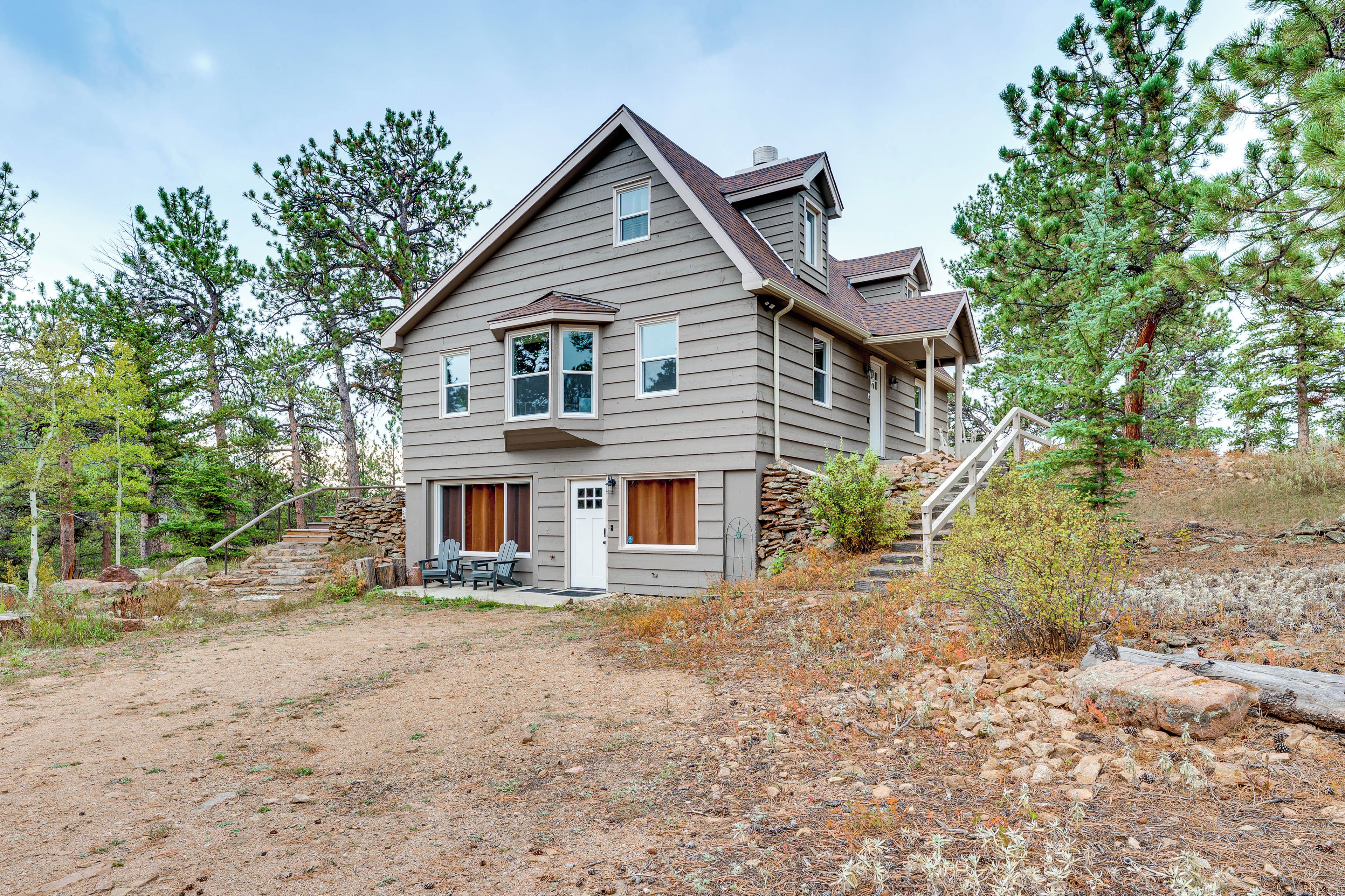 A two-story house with a stone staircase leading to the front door, surrounded by trees and a dry landscape.