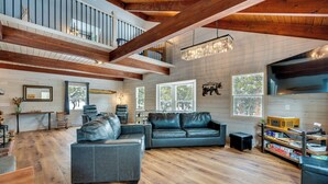 A spacious living room with a large sectional sofa, wooden floors, a staircase, and a chandelier. - Quiet + Peaceful Home in Allenspark w/ Deck! (Allenspark)