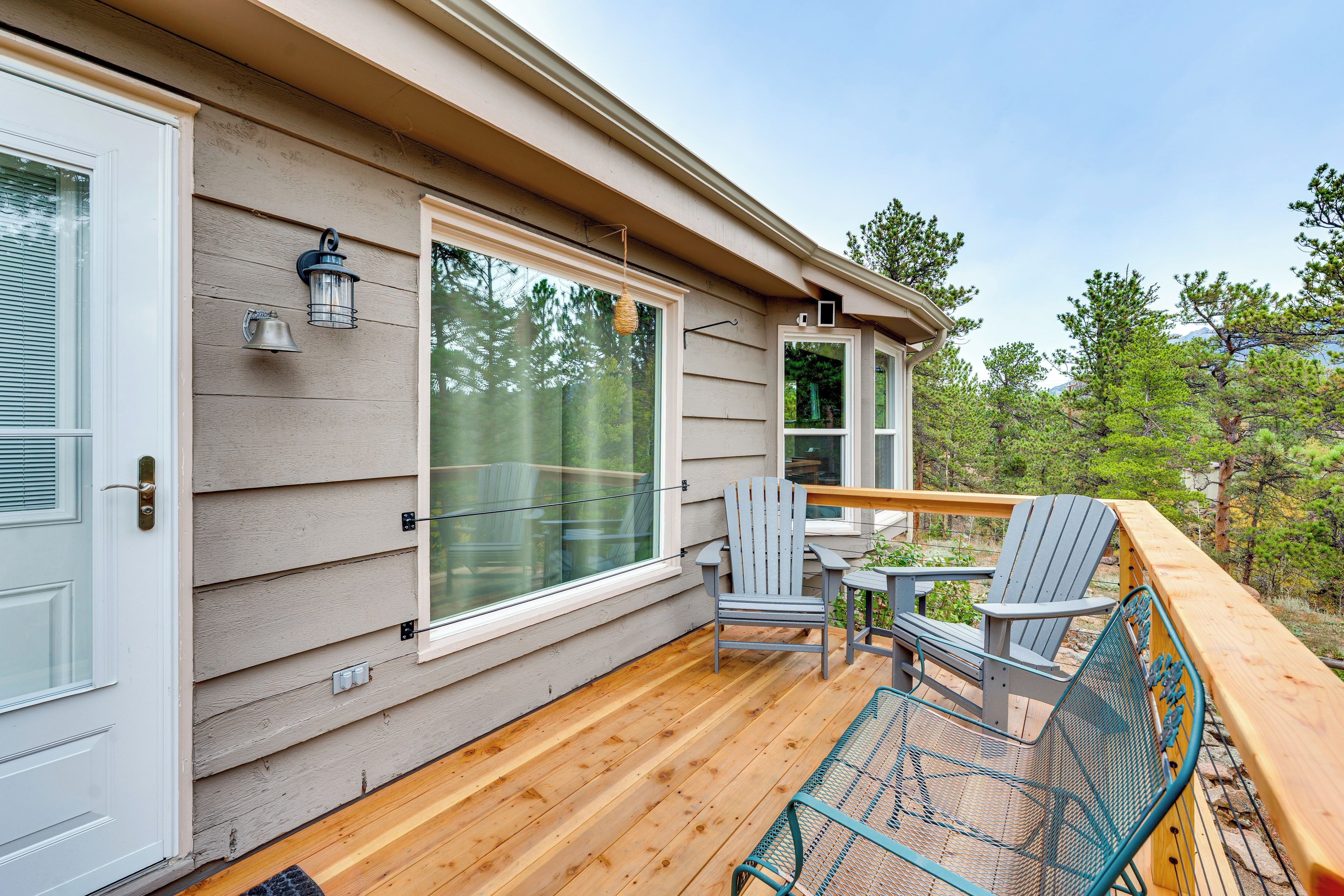 Une terrasse en bois avec des fauteuils Adirondack et une table en métal, donnant sur une zone boisée.