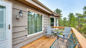 A wooden deck with Adirondack chairs and a metal table, overlooking a forested area.