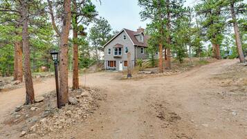 A two-story house with a visible front porch and a dirt driveway leading to it.