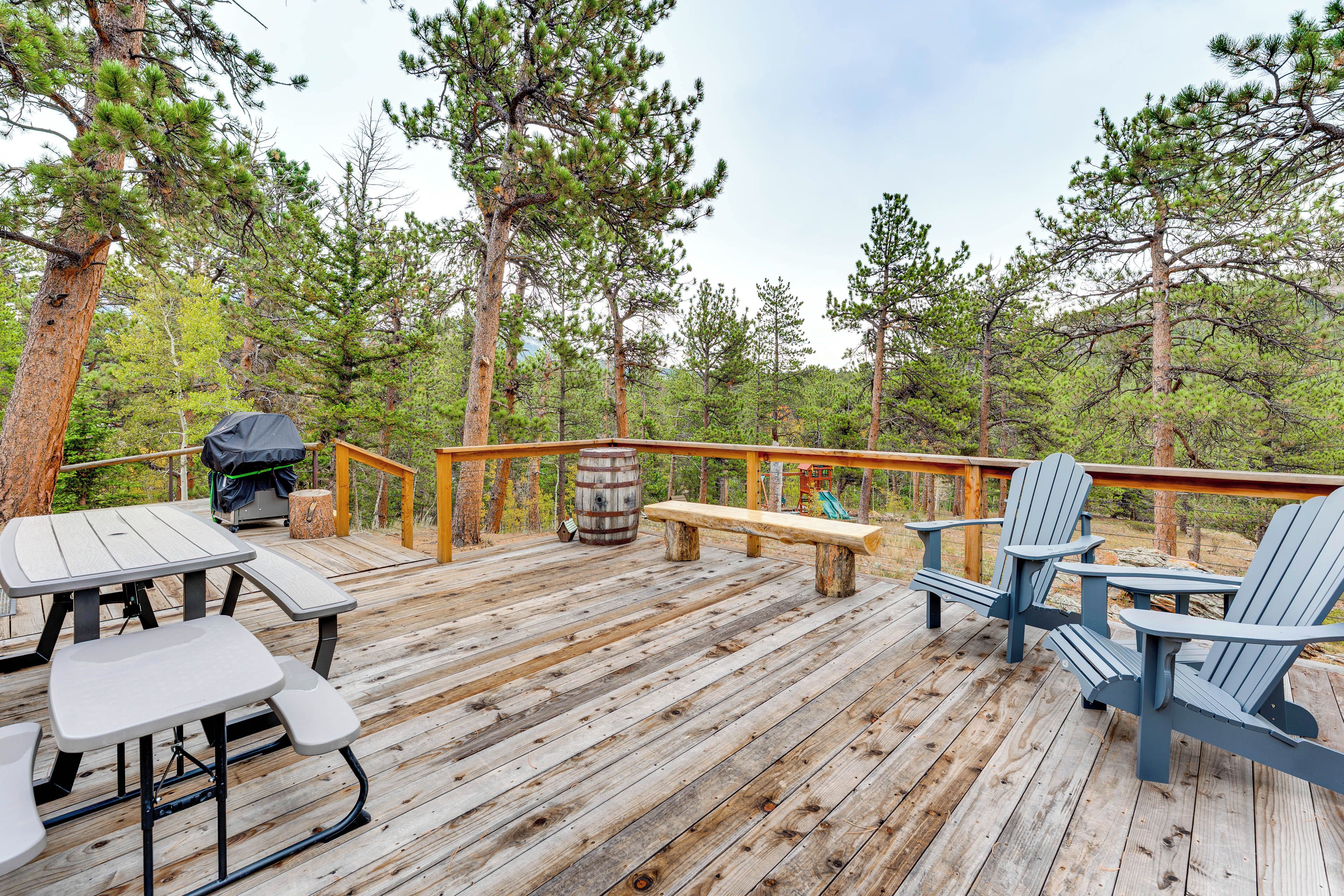 Une terrasse en bois, agrémentée de tables de pique-nique et de chaises Adirondack, entourée d’arbres.