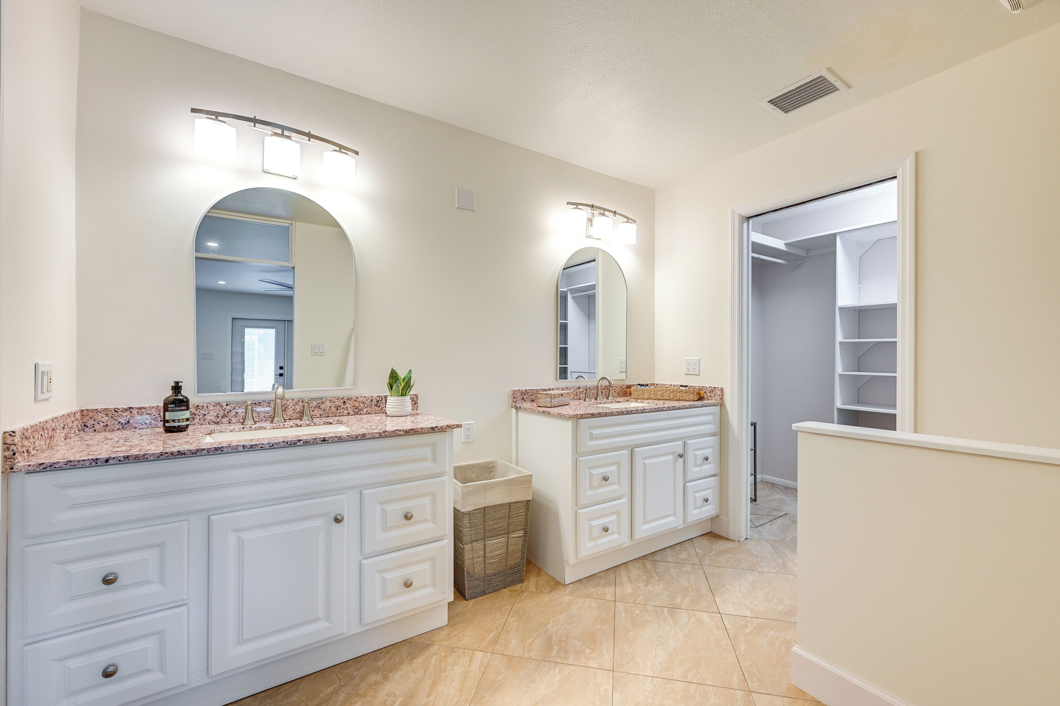 A bathroom with a double vanity, two sinks, a large mirror, and a walk-in closet.