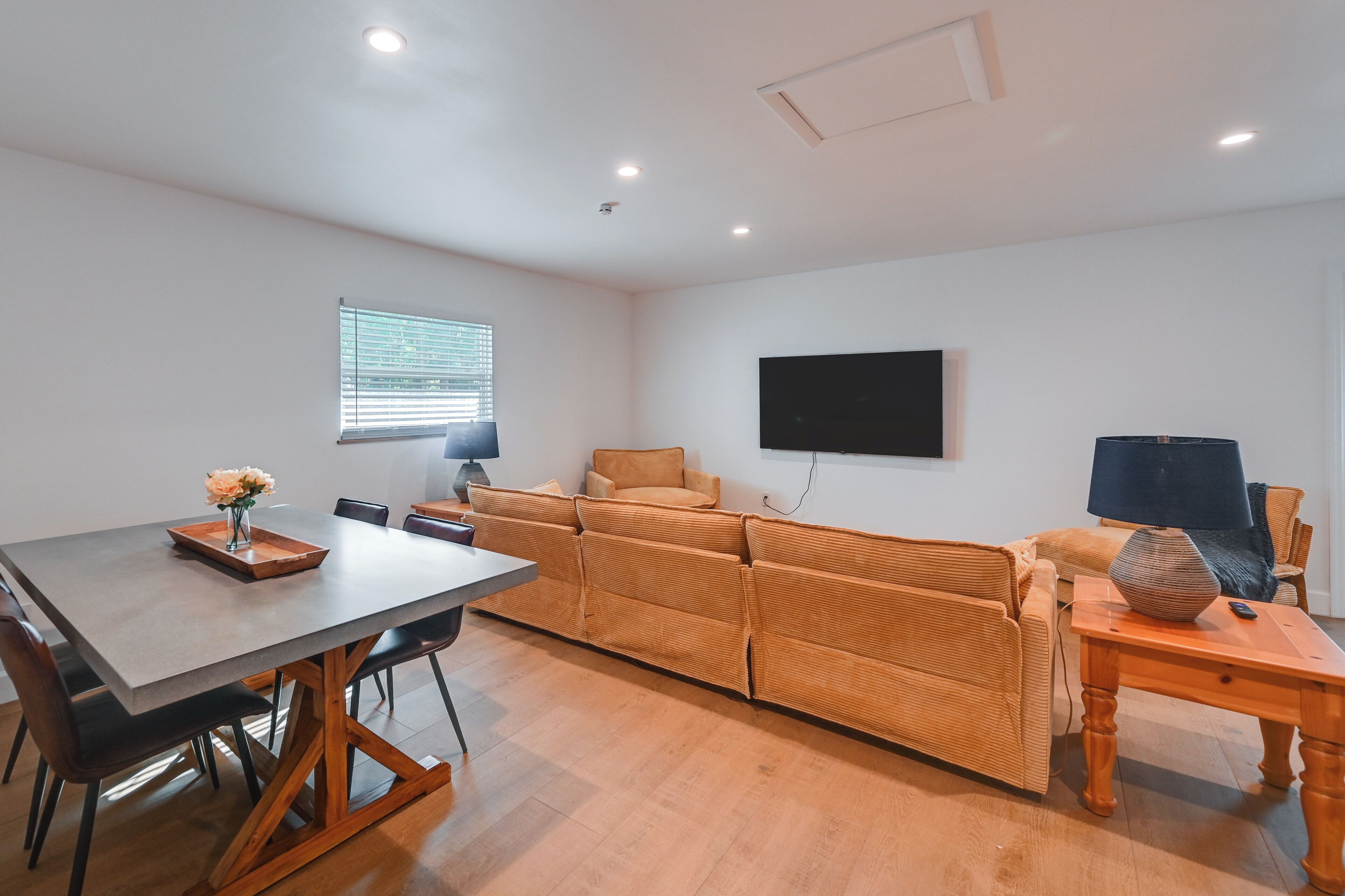 A modern living room with a sofa, a dining table, and a TV mounted on the wall.