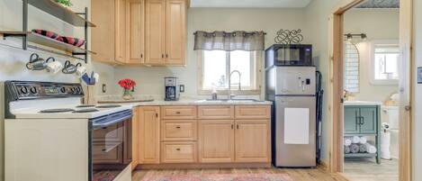 Une cuisine avec des meubles de rangement en bois, une cuisinière, un réfrigérateur et une fenêtre avec un rideau.