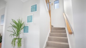A staircase with beige carpeted steps and wooden handrails, leading to a landing with a white wall and a potted plant. - The ultimate property that you need to relax and unwind in Harrintgon (Harrington)