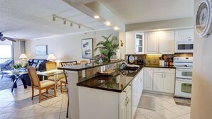 Una cocina moderna con armarios blancos, encimera de granito y comedor con mesa y sillas.