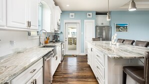 A modern kitchen with white cabinetry, a marble countertop, and a central island.