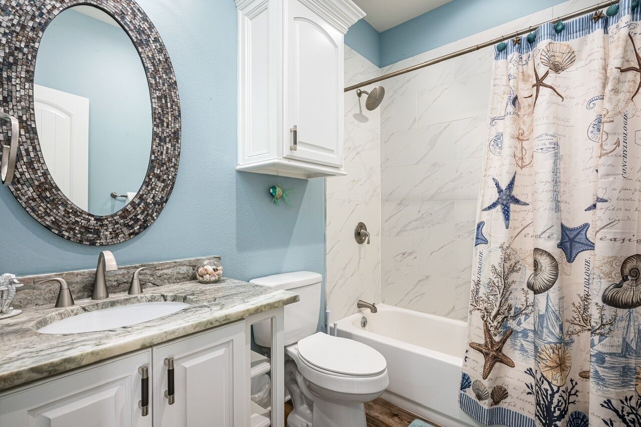 A bathroom with a marble sink, white cabinets, a toilet, and a bathtub.