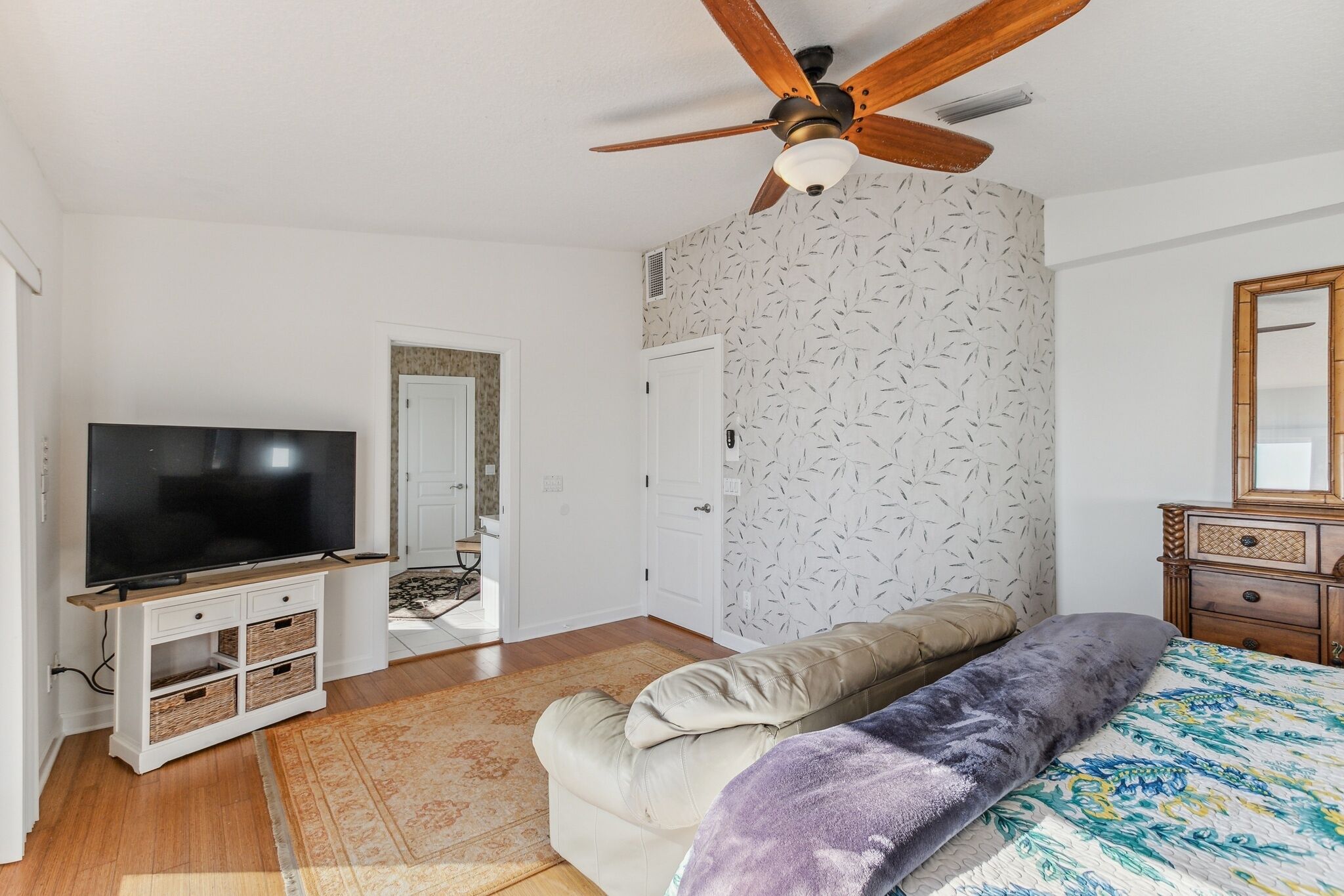 Un dormitorio con cama, televisor sobre un mueble, ventilador de techo, armario y espejo.