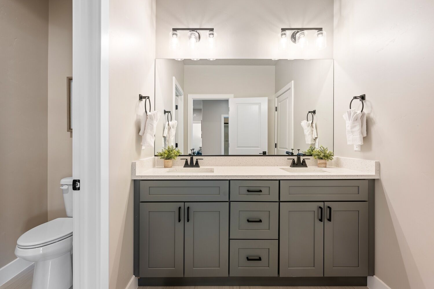A modern bathroom with two sinks, a large mirror, and grey cabinets.