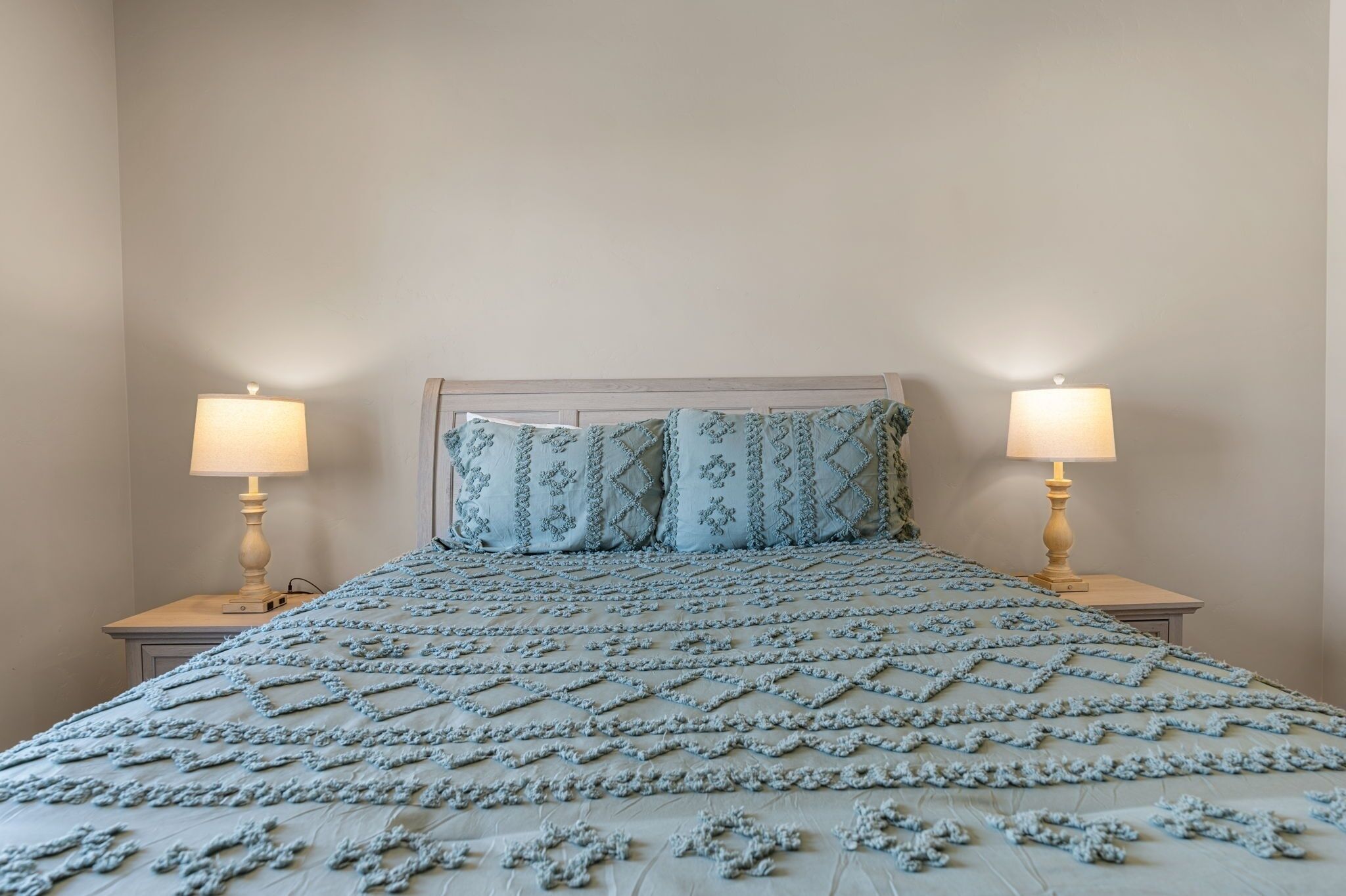 A neatly made bed with a patterned bedspread, two bedside lamps, and matching pillows on a wooden headboard.