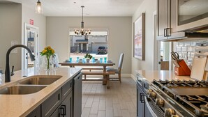 A modern kitchen with a central island, stainless steel appliances, and a dining area with a view to the outside. - Zion's Paradise 6 Bedroom Townhouse (Hurricane)