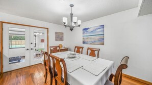 Un comedor con una mesa blanca, sillas de madera, una araña y un cuadro en la pared.