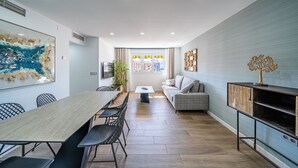 Ein modernes Wohnzimmer mit Essbereich, einer Couch, einem Fernseher und einem Zierbaum auf einem Schrank.