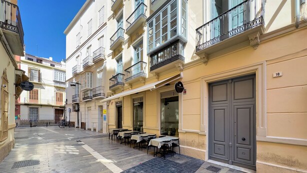 Una calle estrecha con mesas al aire libre, un restaurante y un edificio con una puerta cerrada.