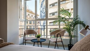Ein Schlafzimmer mit großem Fenster, zwei Stühlen, einem kleinen Tisch und einem Blumentopf.