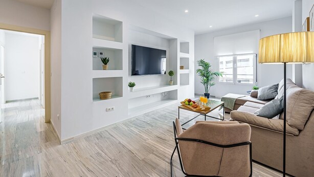 Ein modernes Wohnzimmer mit Flachbildfernseher, Einbauschränken, einer Couch, einem Couchtisch und einer Lampe.