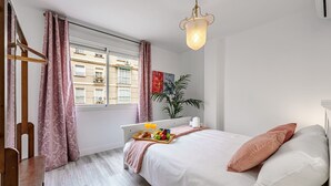 Un dormitorio con cama, mesita de noche y ventana con cortinas.