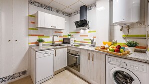 Una cocina moderna con muebles blancos, lavavajillas, horno, microondas y lavadora.