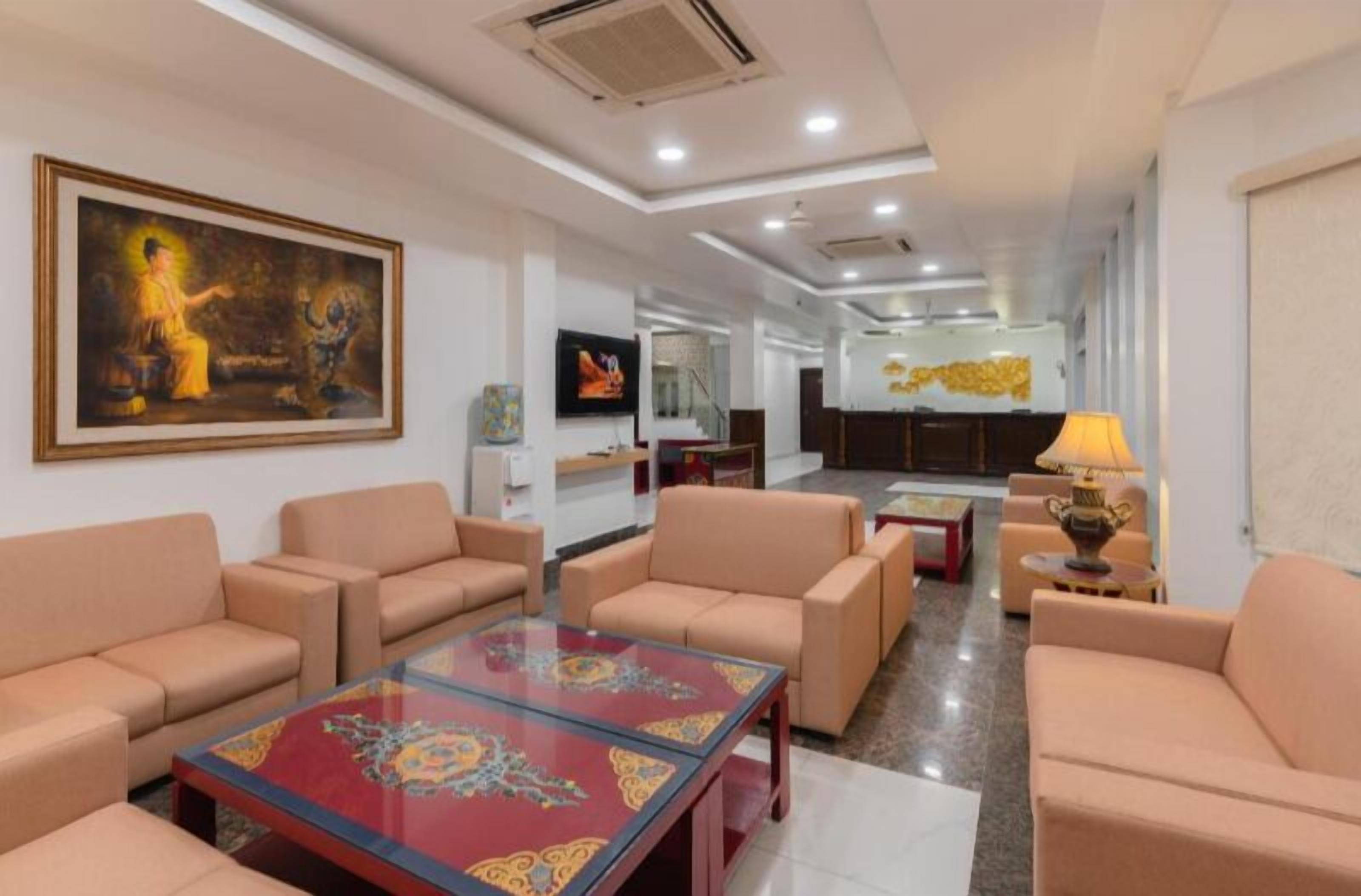 A hotel lobby with beige sofas, a glass coffee table, a television, and a painting on the wall.