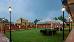 Un patio con una carpa blanca, mesas y sillas, rodeado de muros de ladrillo y faroles.