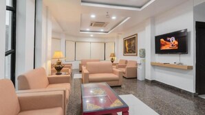 Habitación de hotel moderna con sofás beige, una mesa de centro roja, un televisor de pantalla plana y un cuadro en la pared.
