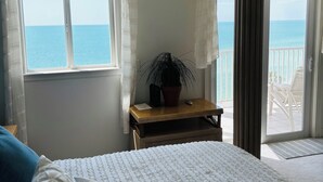 A bedroom with a large bed, a nightstand, a potted plant, and a view of the sea through a balcony door. - Direct large, beachfront Condo, steps to Vanderbilt Beach, 3 bedroom, 3 bath. (Naples)
